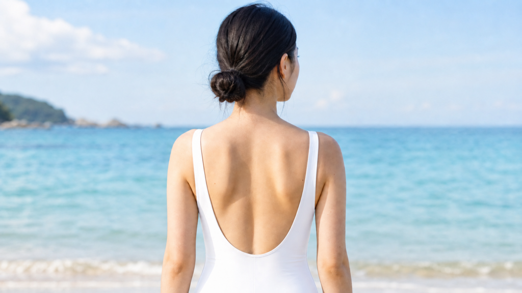 海を背景に二の腕から肩と背中のラインを見せる水着姿の女性