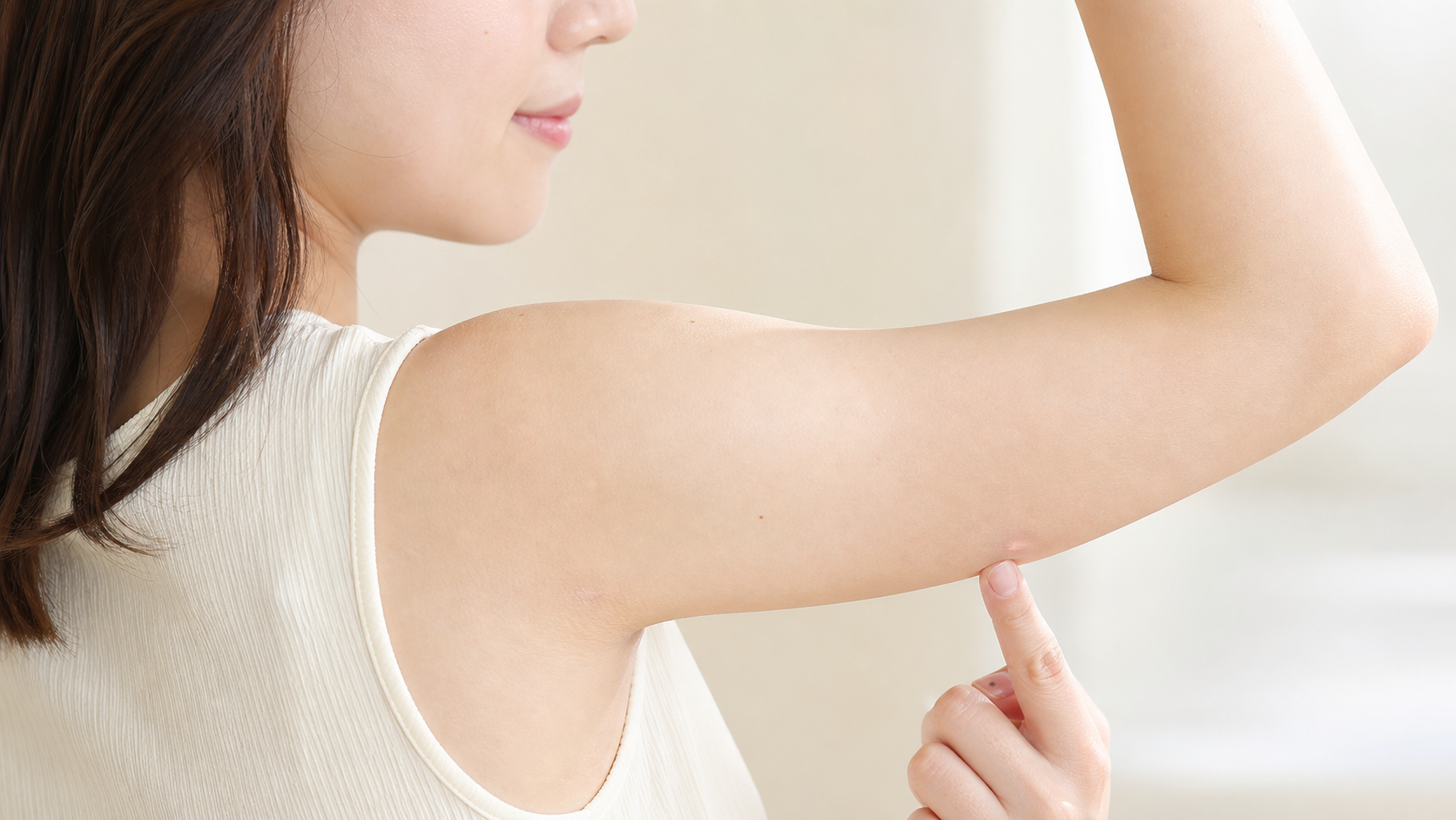 二の腕脂肪吸引後の小さな傷跡を指で確認する女性